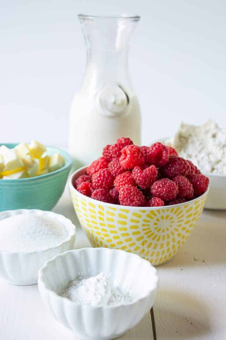 Fresh raspberries in a bowl along with flour, sugar, butter, milk and baking powder.