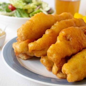 Stacks of crispy golden fish on a white plate with a blue rim.