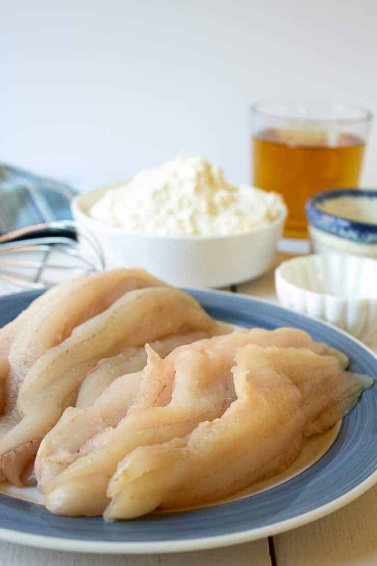 White fish fillets with flour and beer behind the fish. 