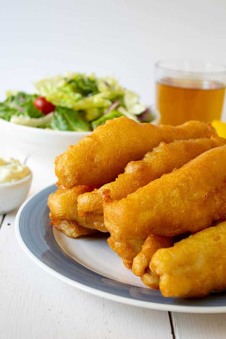 A blue and white plate stacked full of fried fish. 