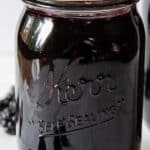 A glass canning jar filled with jam and fresh blackberries around the jar.