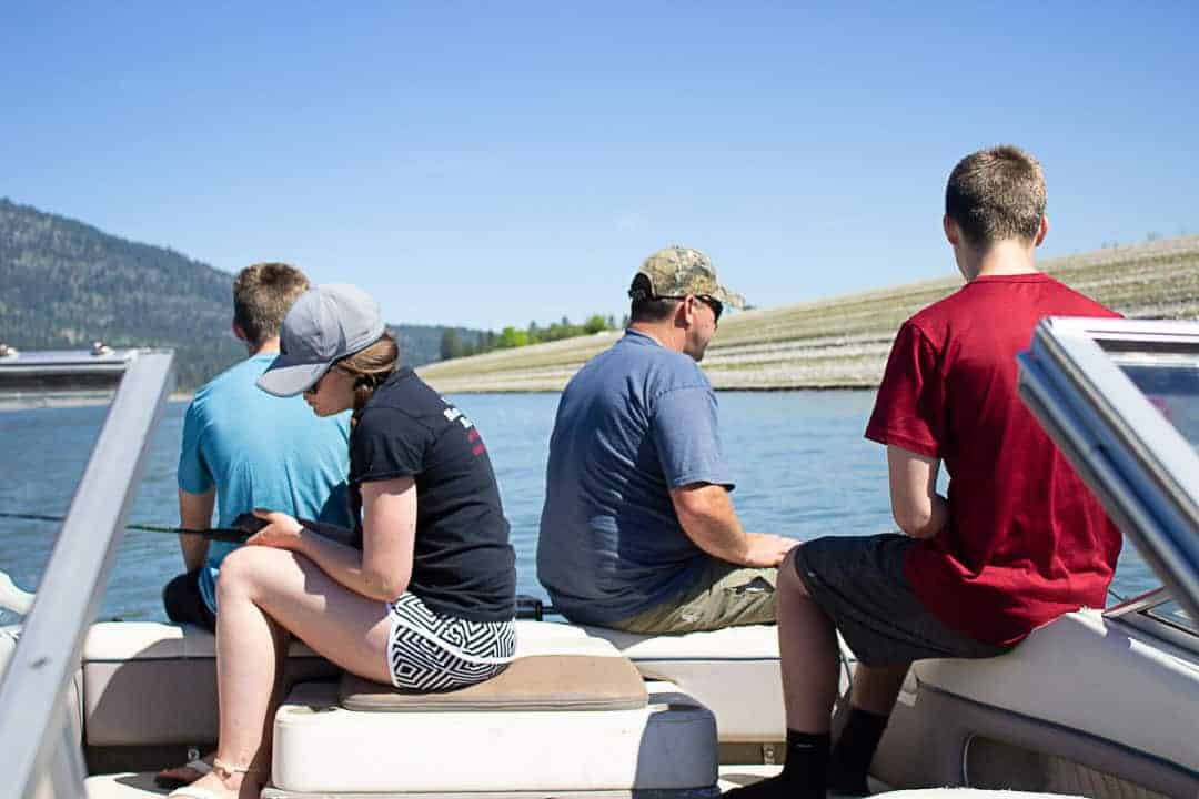 Four people sitting on a boat with fishing poles.