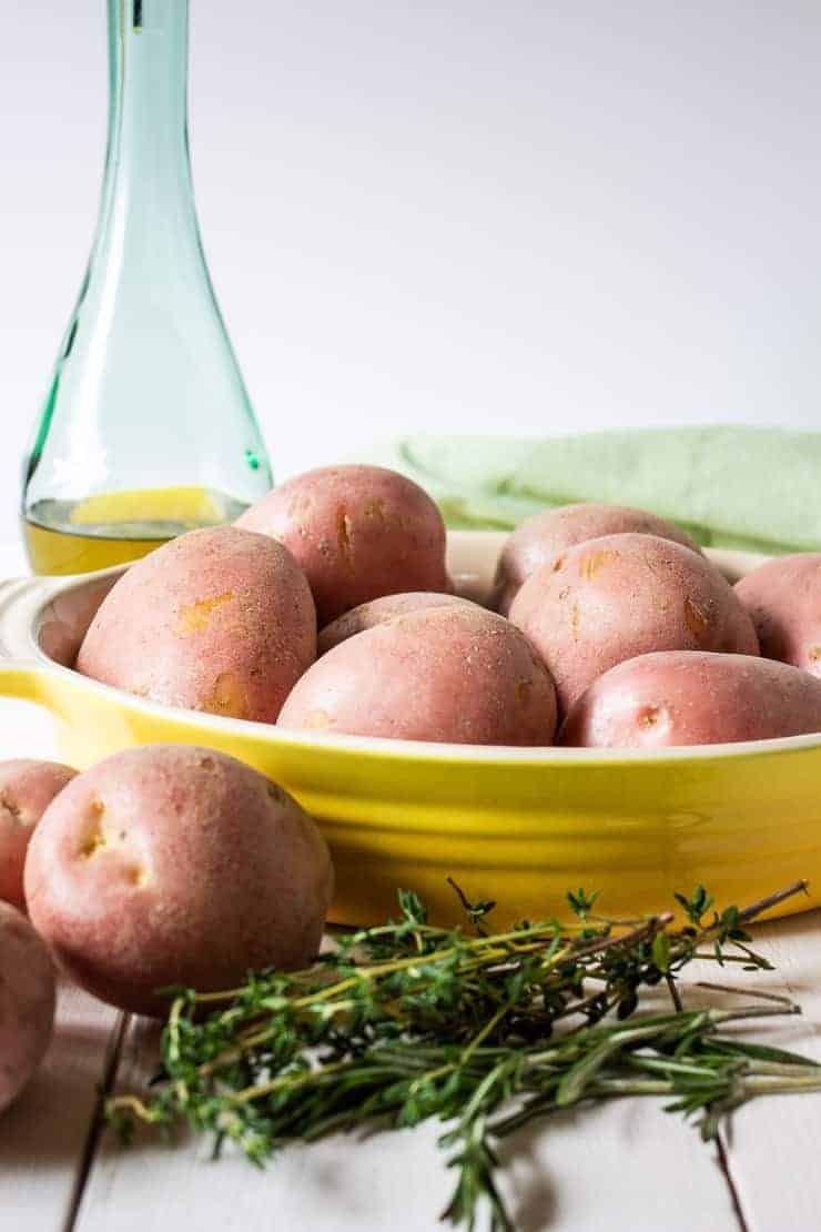 Red potatoes and fresh herbs all piled around a yellow dish.