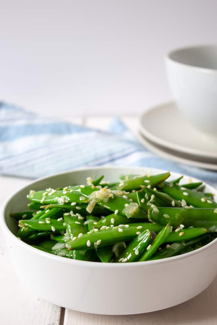 A bowl full of sauteed sugar snap peas topped with sesame seeds.