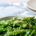 A white bowl filled with fresh pea pods topped with sesame seeds.