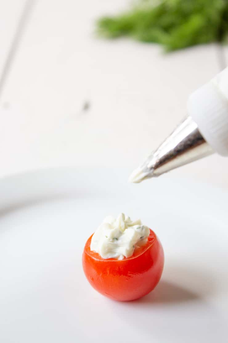 Piping a cream cheese filling into a cherry tomato.