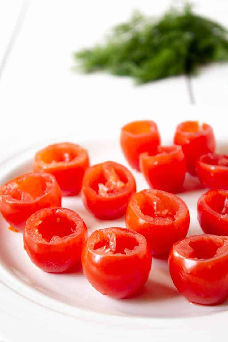 Seeded cherry tomatoes on a white plate with fresh dill in the background.