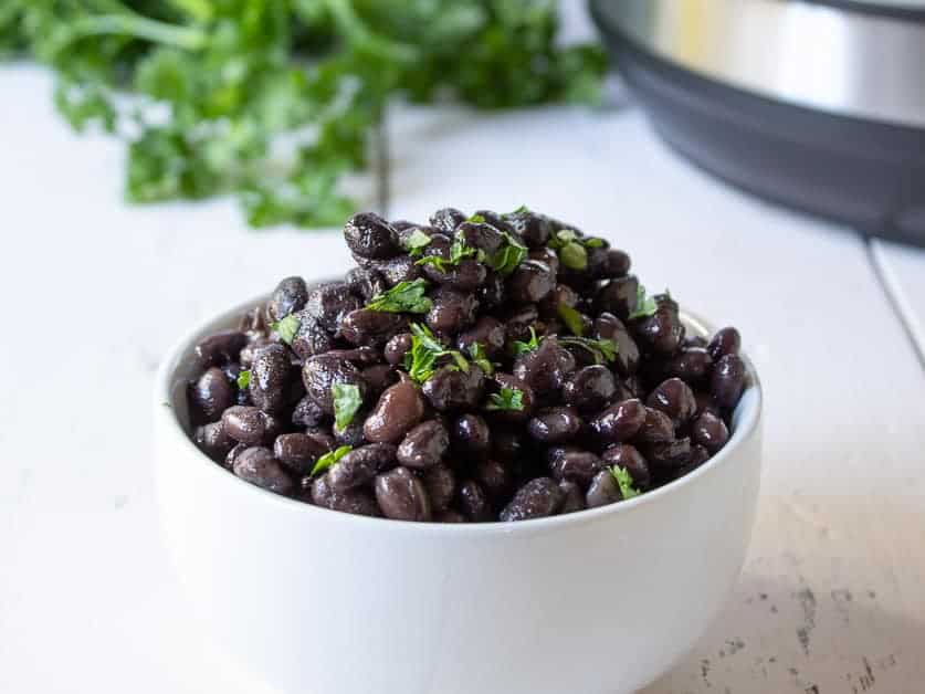 A white bowl filled with black beans topped with chopped parsley.