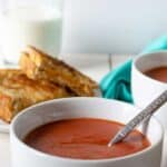 A bowl filled with tomato soup with a spoon in the bowl.