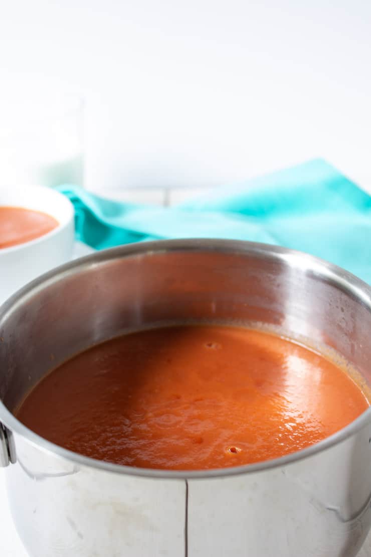 A pot full of creamy tomato soup with a turquoise napkin in background.