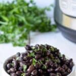 Black beans in a white bowl topped with finely chopped green herbs.