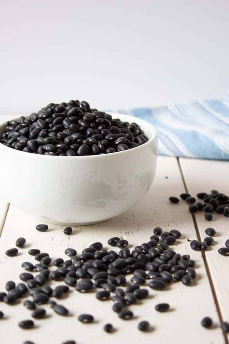 Dried black beans in a bowl and spread on a white board.