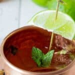 A copper mug filled with a clear beverage and topped with a fresh sprig of mint.