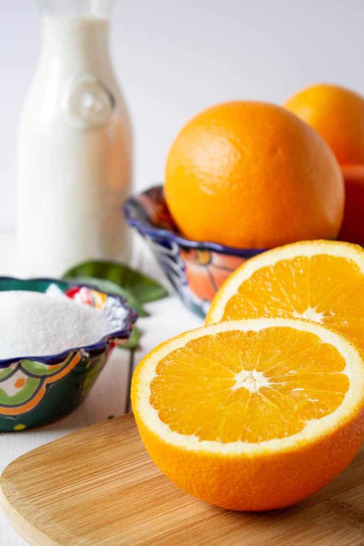 Fresh oranges cut in half, sugar and milk displayed on a white board.