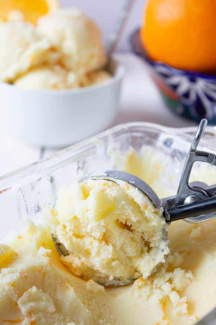 An ice cream scoop scooping up some orange ice cream.