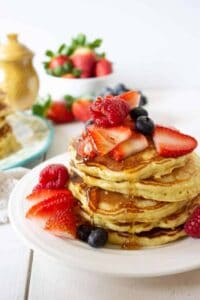Four pancakes stacked and topped with fresh strawberries, raspberries and blueberries.