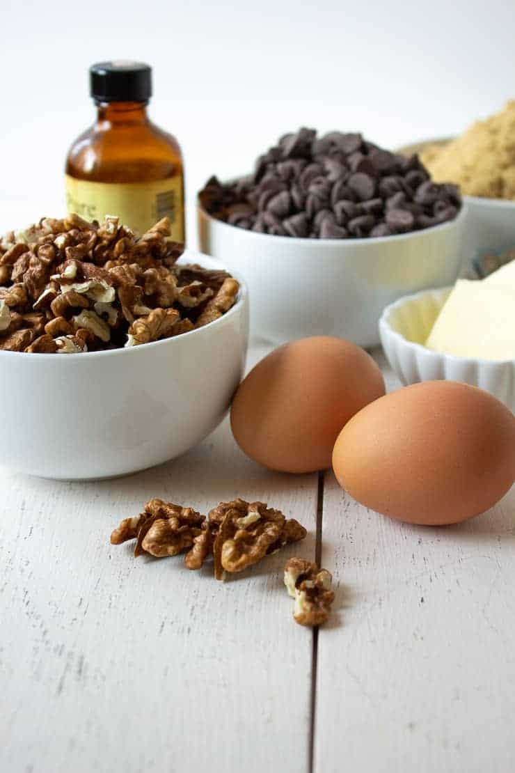 White bowls filled with walnuts, chocolate chips and butter along with eggs and vanilla.