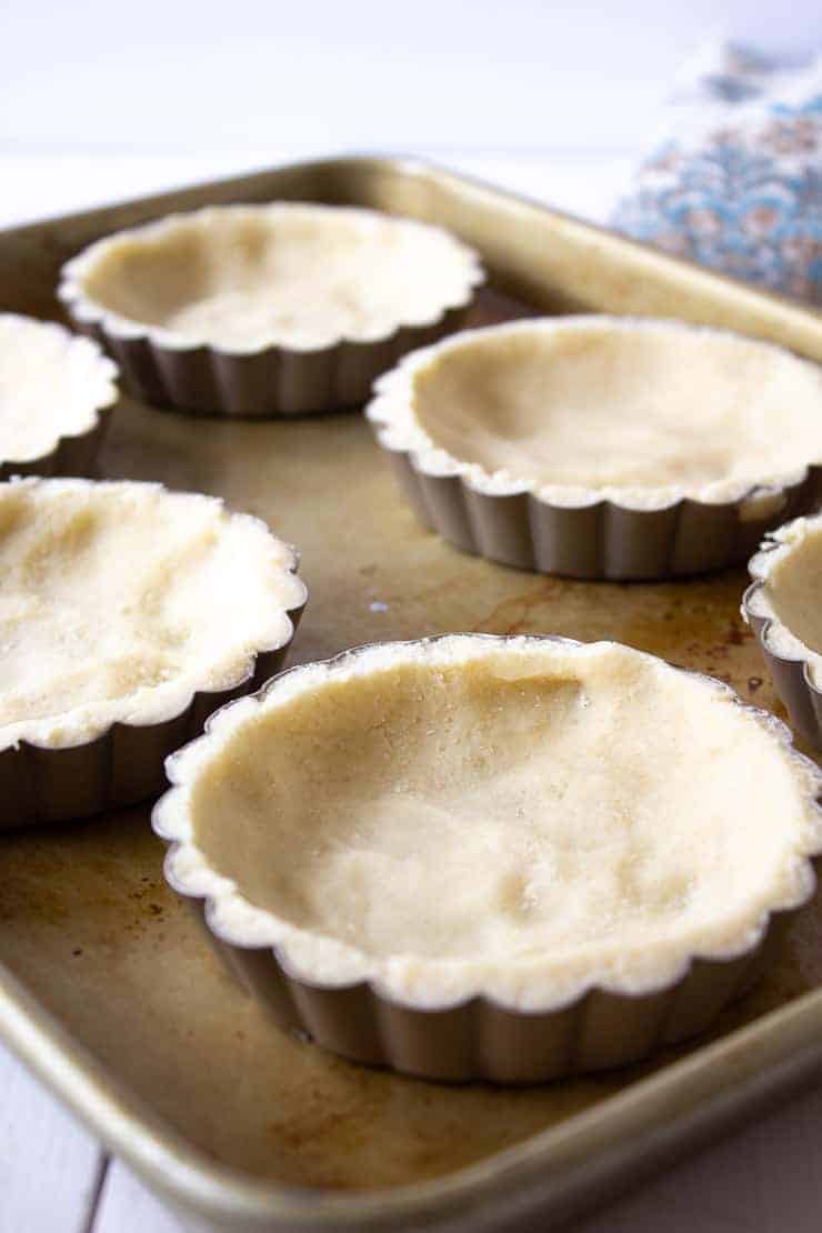 Pastry crusts in mini tart pans on a baking sheet.