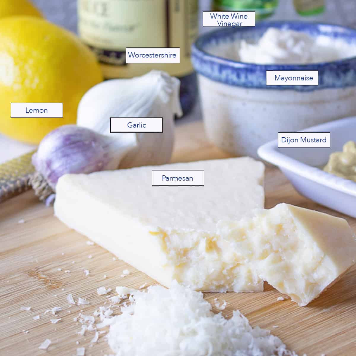 Grated parmesan cheese on a wooden cutting board with other ingredients behind the cheese.