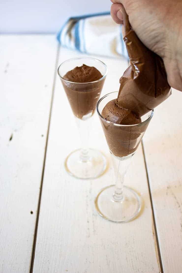 Pipping chocolate mousse into small cordial glasses.