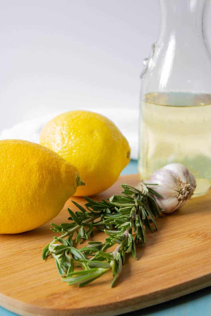 Fresh lemons, rosemary, garlic and white wine on a cutting board.