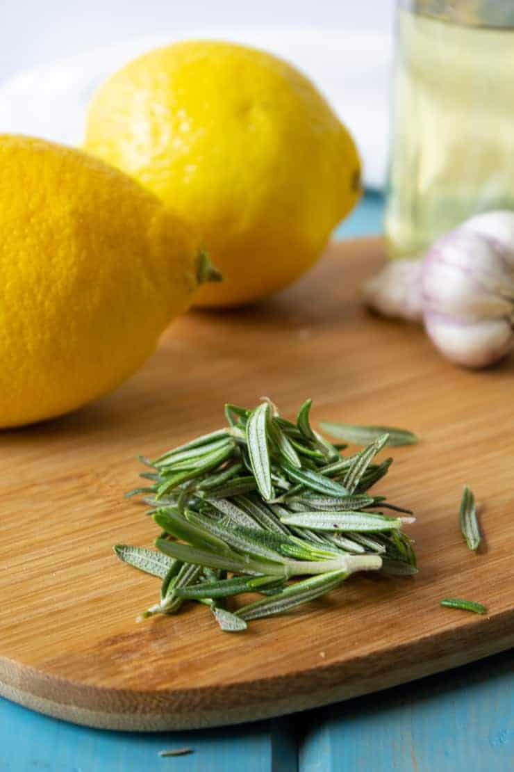 Fresh rosemary with fresh lemons and garlic on a cutting board.