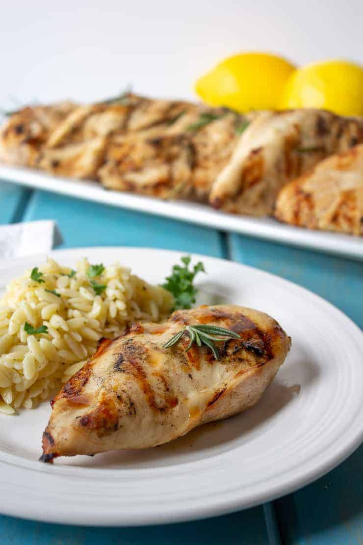 A grilled chicken breast on a white plate with orzo pasta next to the chicken.