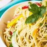 Spaghetti noodles with cucumbers and peppers topped with fresh basil in a white bowl.