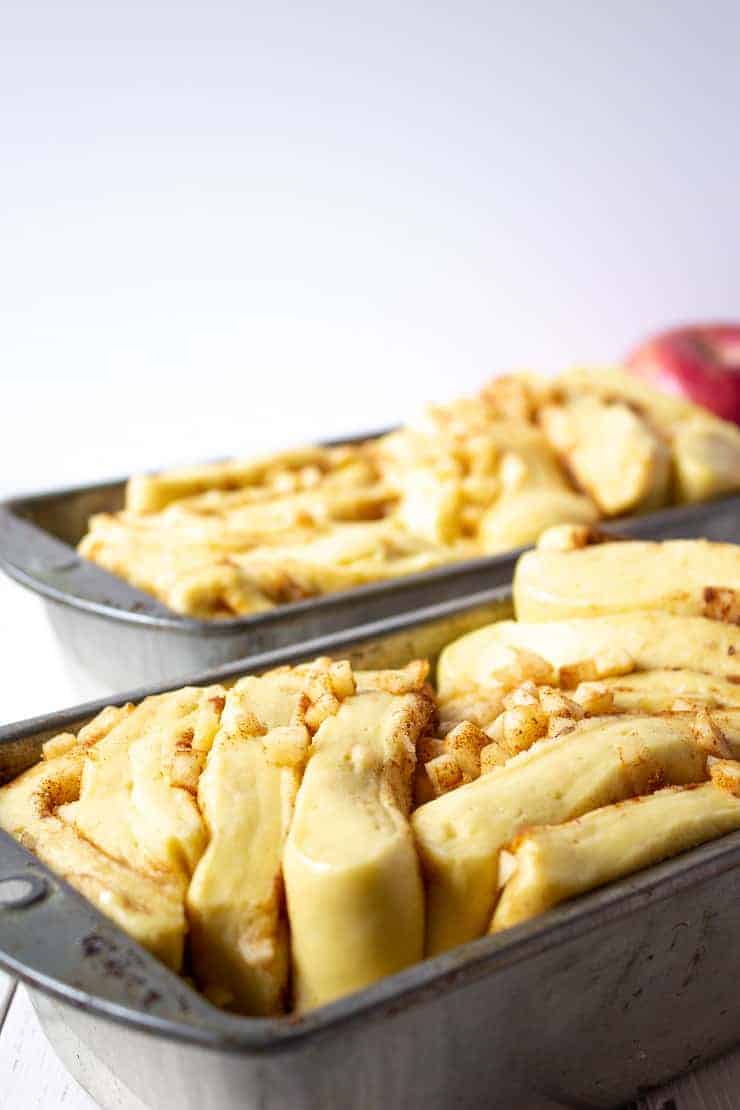 Layers of dough with chunks of apples in a bread pan.