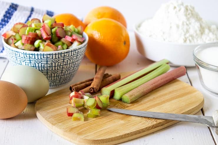 Rhubarb stalks being cut into small pieces on a wooden cutting board.