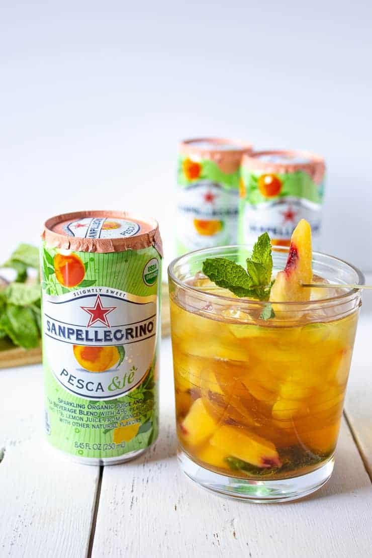 Sparkling Lemon Peach Teach in a glass filled with ice next to a can of Sanpellegrino.