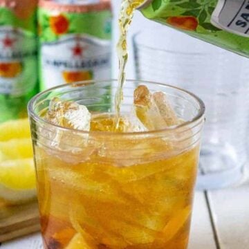 Sparkling tea being poured into a glass filled with ice, peaches, and mint.