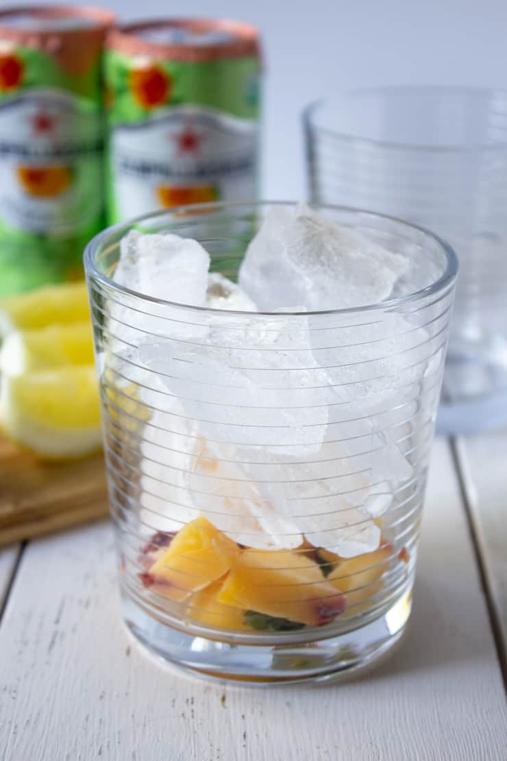 A glass filled with ice, chopped peaches, mint and lemon juice.