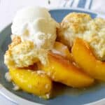 Peach slices topped with a cobbler topping and a scoop of vanilla ice cream.