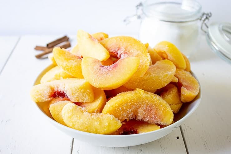 A white bowl filled with frozen peach slices.