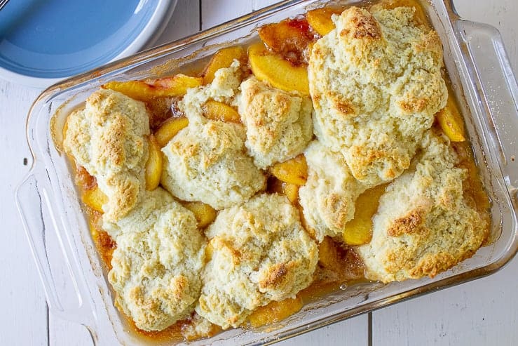 A glass baking dish filled with peaches and topped with a cobbler biscuit.