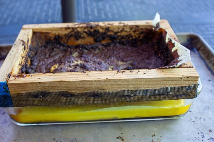 Yellow beeswax in a glass dish with a wooden screen over dish.