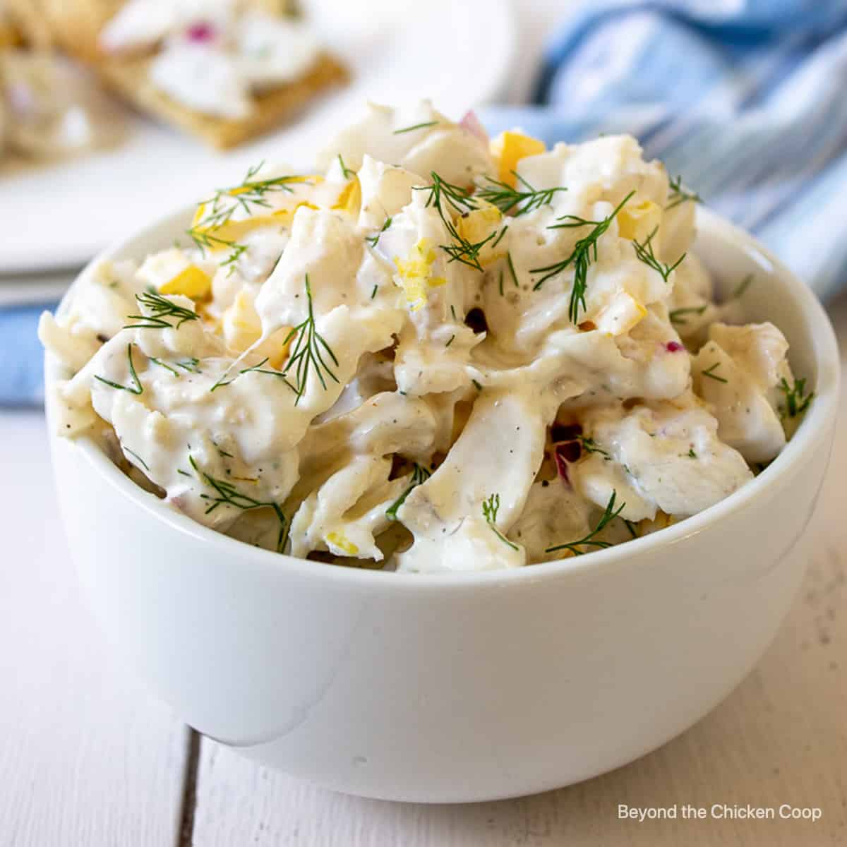 A white bowl filled with fish salad topped with fresh dill.