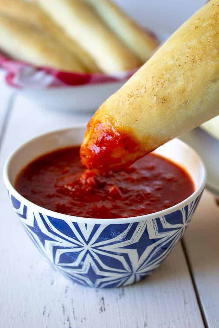 Breadstick being dipped into marinara sauce. 