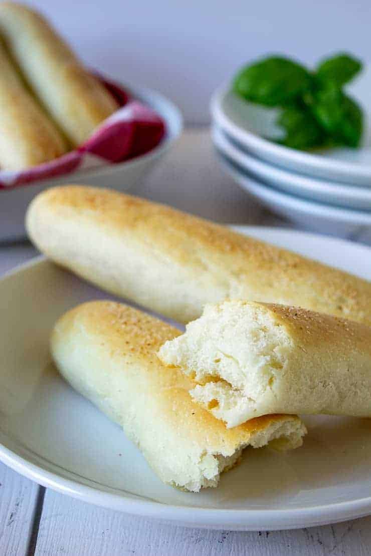 Bread sticks on a white plate with one bread stick torn in half.