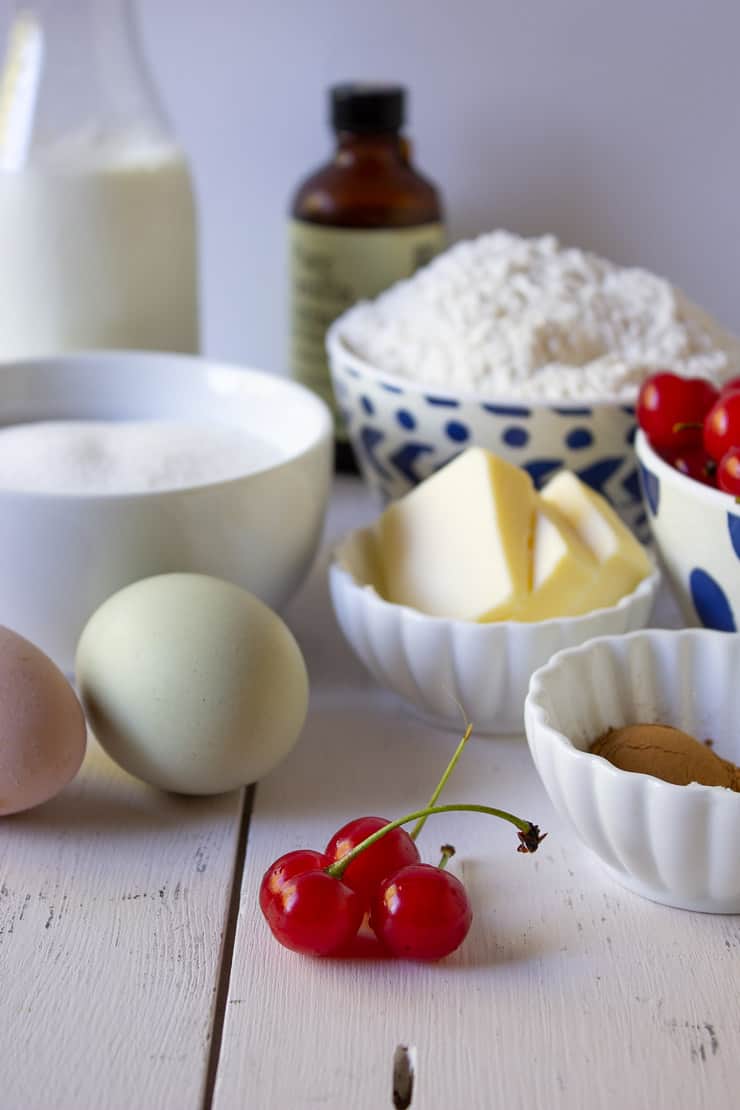 Fresh cherries, eggs, butter, flour and sugar on a white board.