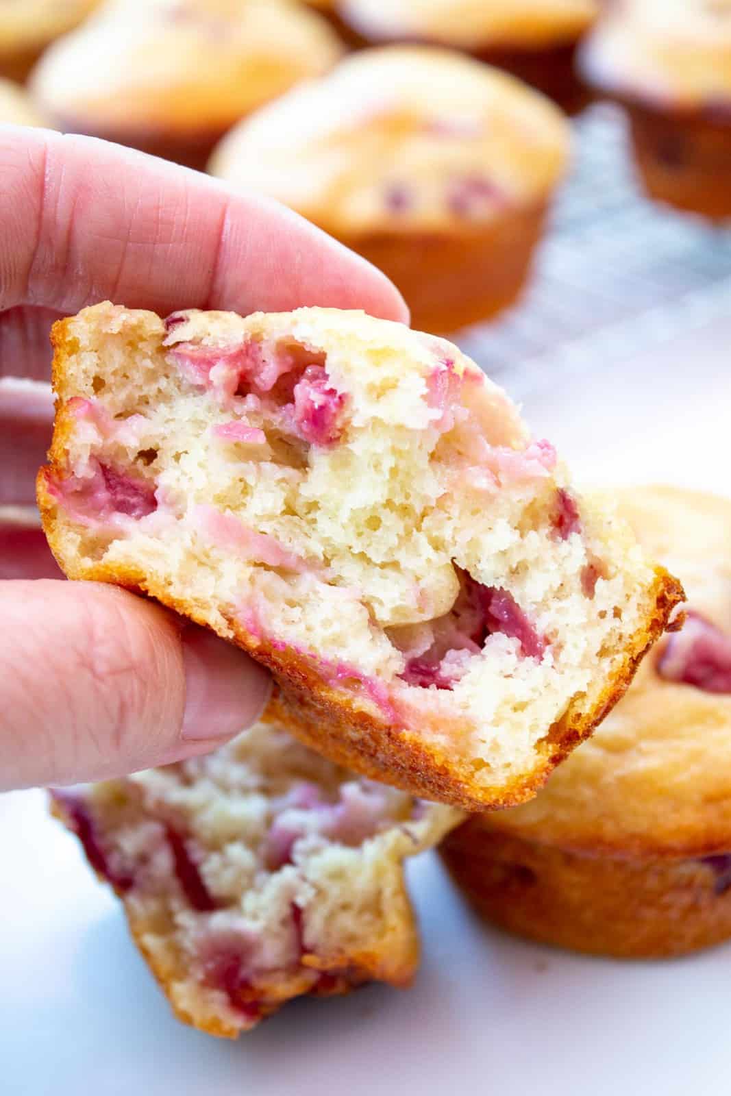A half of a muffin filled with cherries held in one hand.