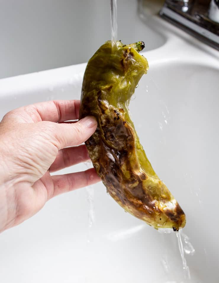 A roasted anaheim pepper held under running water in the sink. 