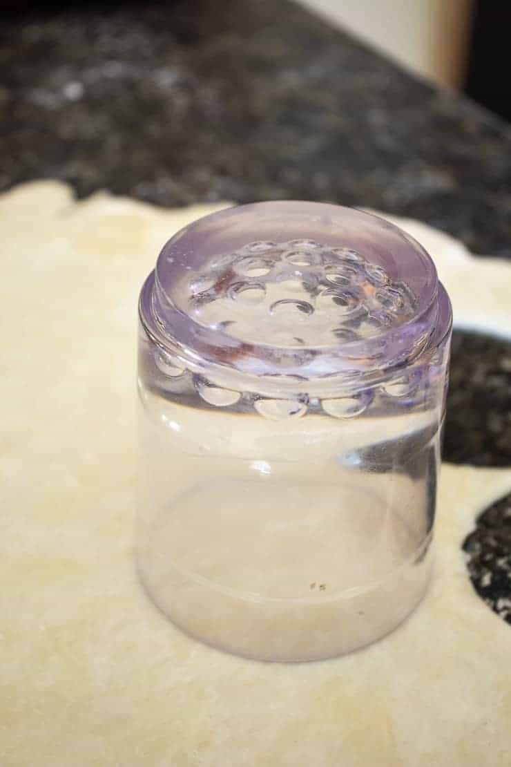 Pie crust dough being cut into small circles with an inverted glass.