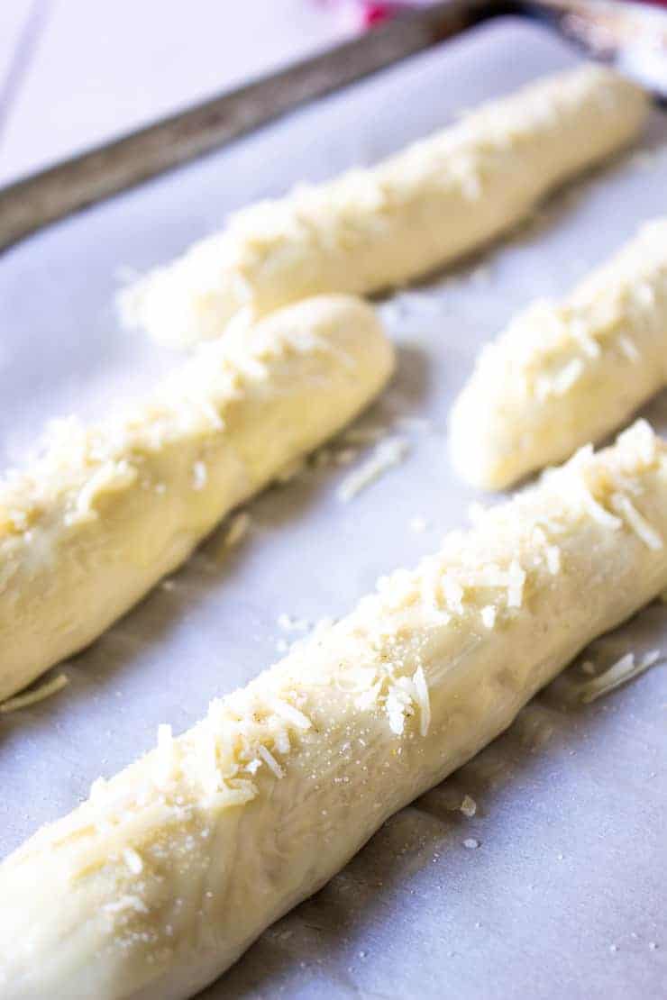 Shredded Parmesan cheese sprinkled on breadsticks dough.