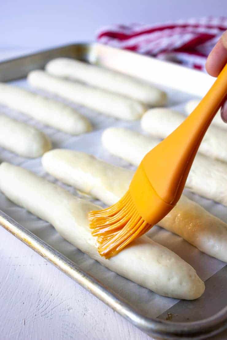 An orange pastry brush spreading butter on raw bread dough. 