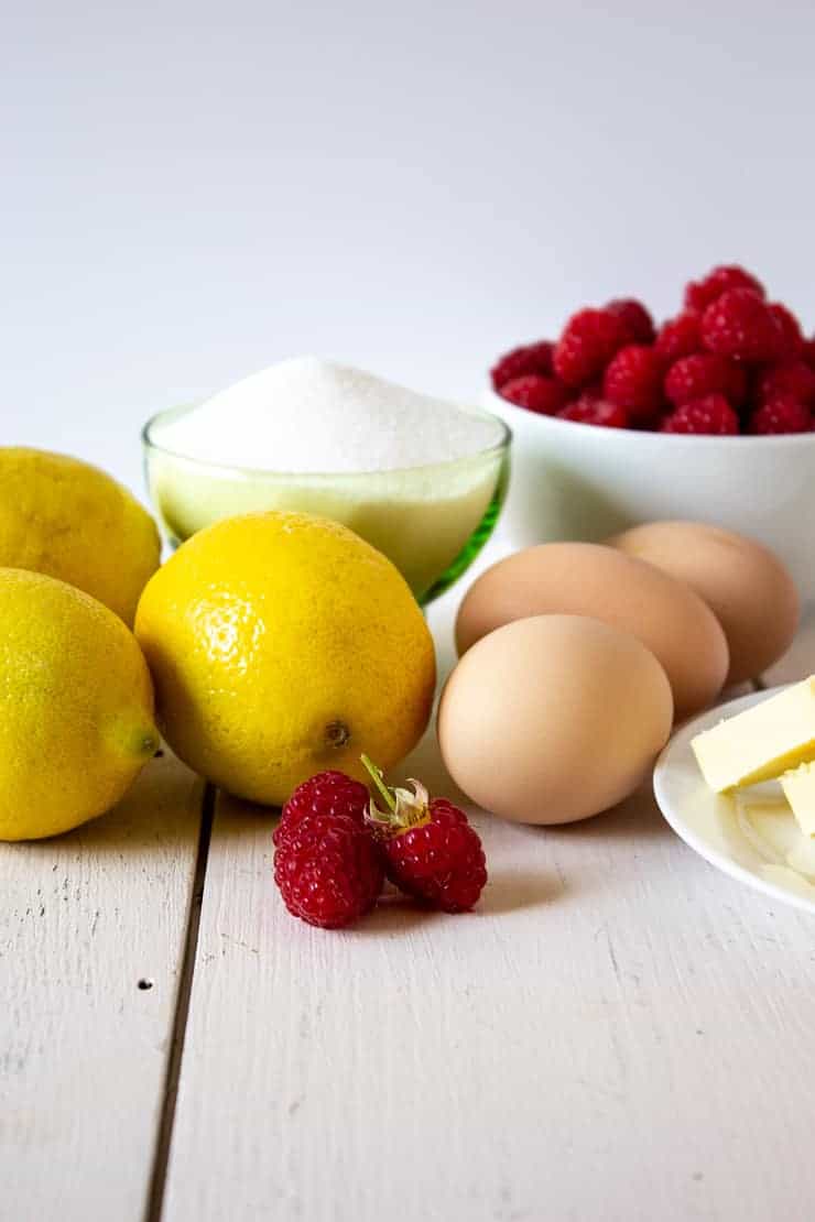 Fresh raspberries with lemons, eggs, sugar and butter all displayed on a white board. 