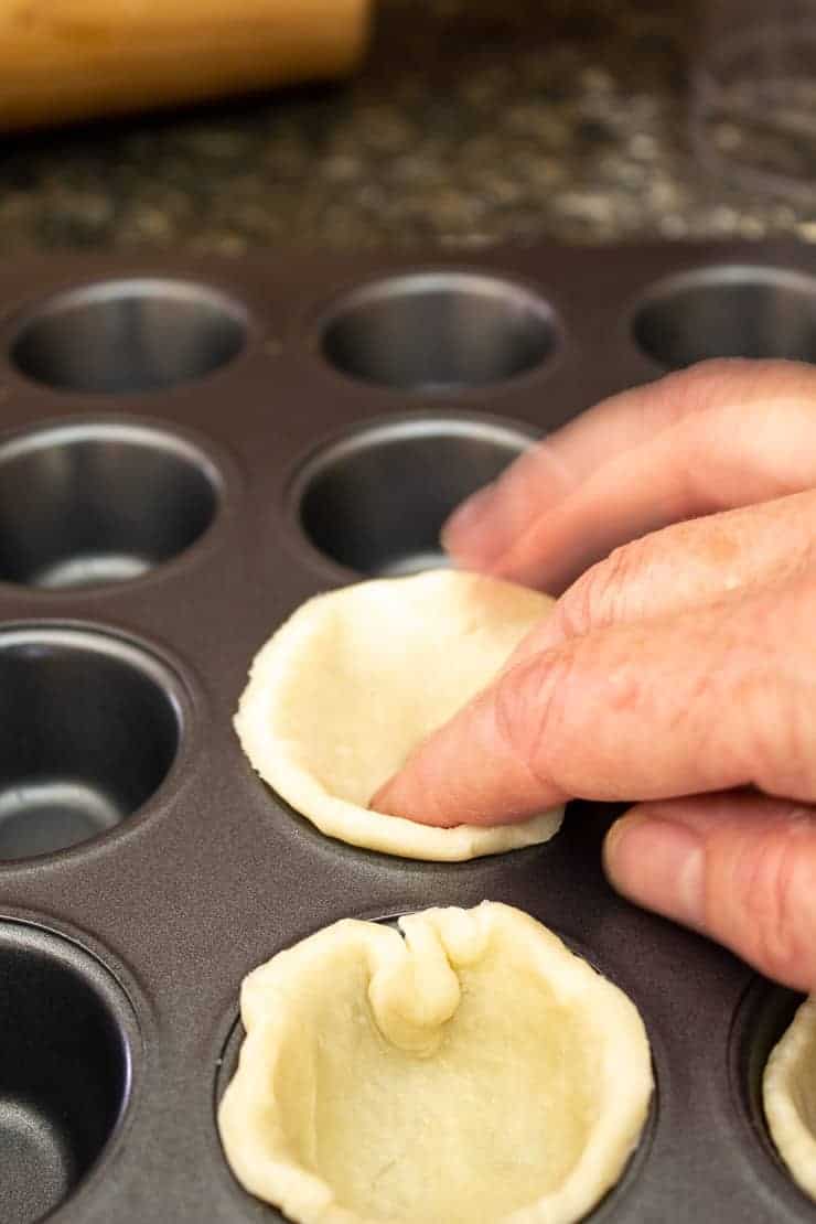 Placing pie crust dough into a mini muffin tin.