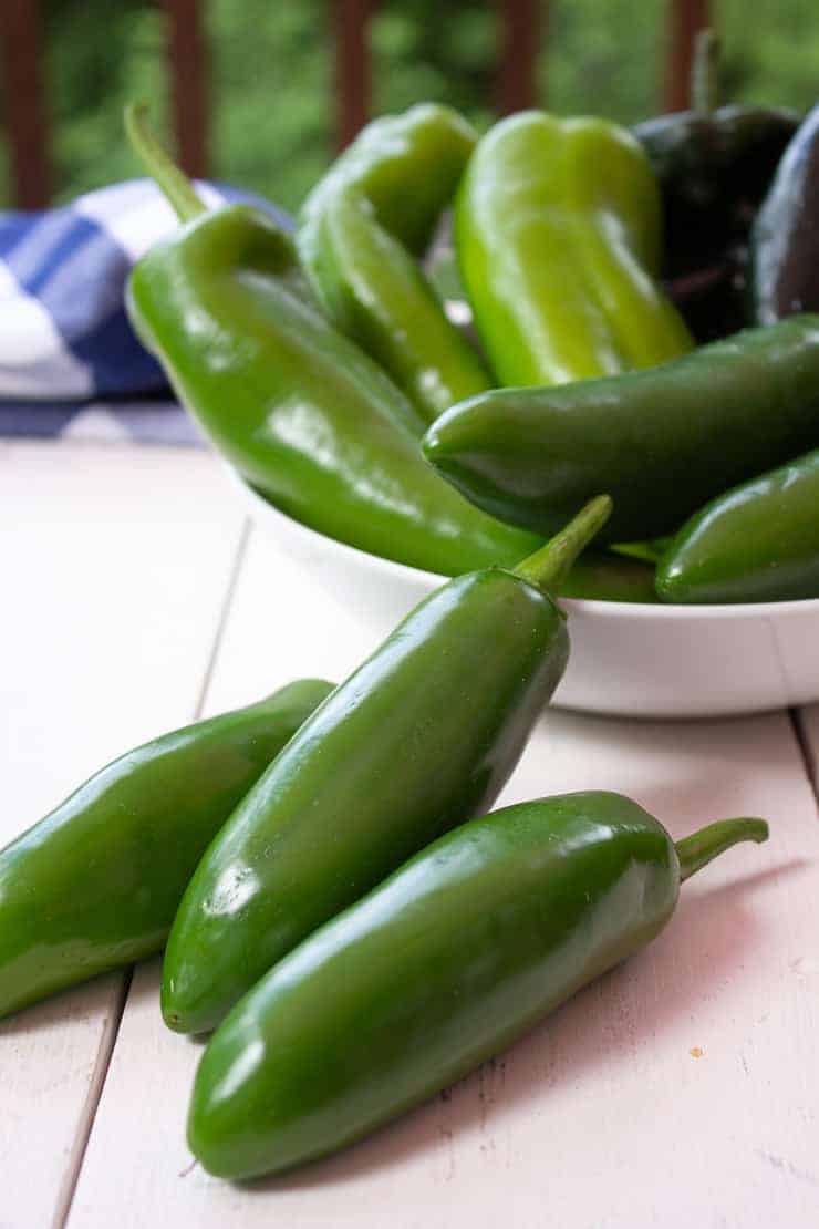 Fresh jalapenos, anaheims and poblano peppers in a white bowl. 