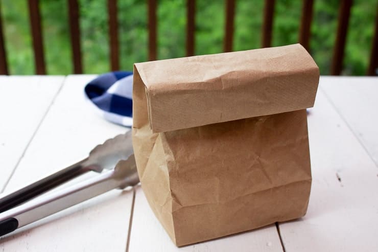 A paper bag on a white board with a a pair of tongs next to the bag. 